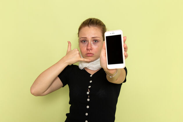 疾病正面图年轻女性感觉很不舒服 拿着手机在淡绿色的墙上生病了持有年轻人光
