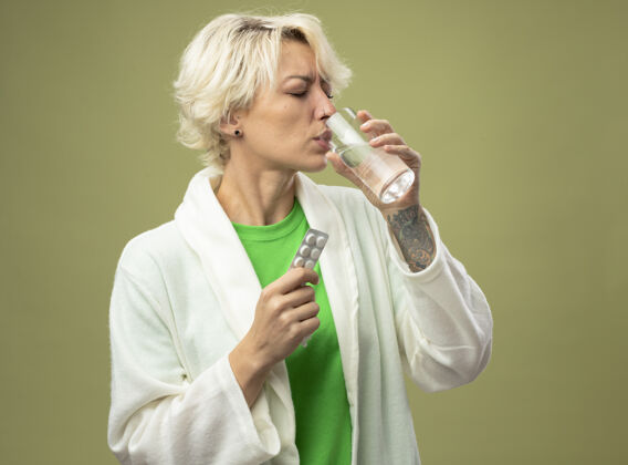 药一个短发女人站在光墙上 手里拿着一杯吃药的水 感觉不舒服服用女人光