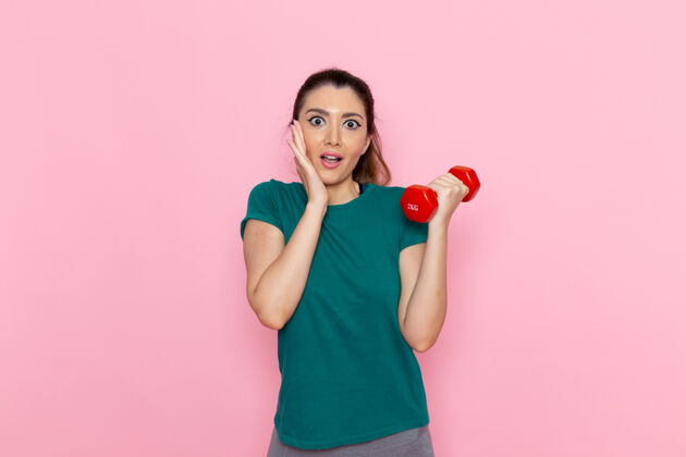 观点正面图年轻女性手持哑铃在浅粉色墙上运动员运动锻炼健康锻炼前面锻炼运动