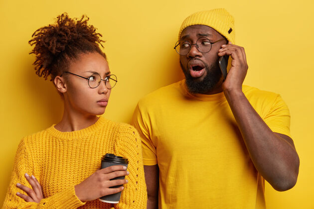 眼镜心烦嫉妒的非洲裔妻子看着用手机说话的丈夫电话毛衣女性
