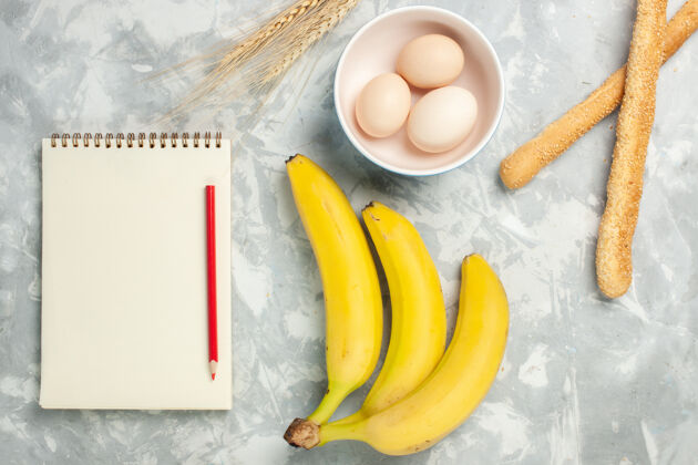 浅白色顶视图：生鸡蛋放在小盘子里 面包和香蕉放在浅白的桌子上 生食物 早餐 水果面包可食用的水果整个里面