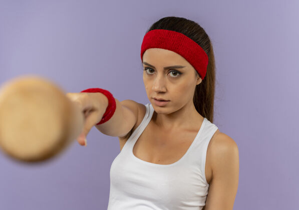 指向身穿运动服的年轻健身女 头戴棒球棒指着镜头 严肃的脸站在灰色的墙上头带女人运动员