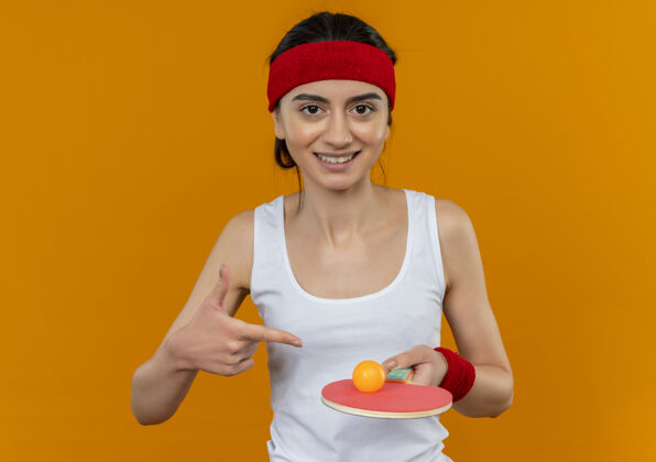 网球穿着运动服的年轻健身女士 头上带着球拍和乒乓球头带姿势球拍