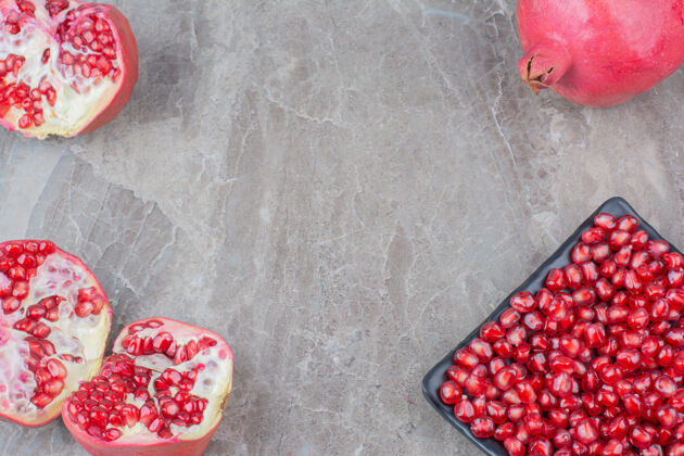 新鲜红石榴和一盘种子在石头的背景上水果红色种子