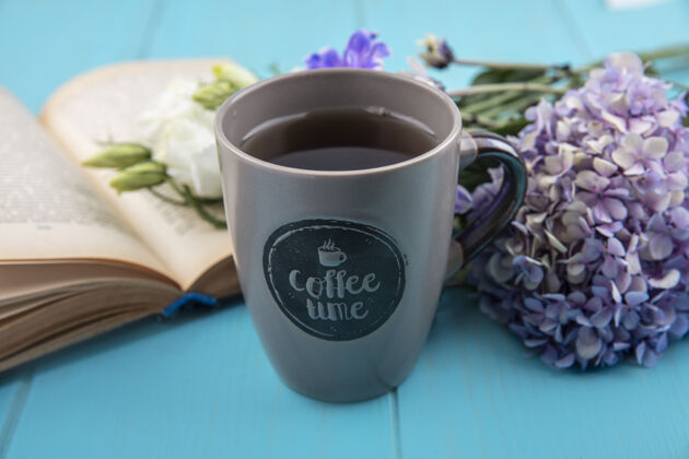 杯子一杯咖啡的侧视图 蓝色背景上有鲜花和打开的书花咖啡馆书