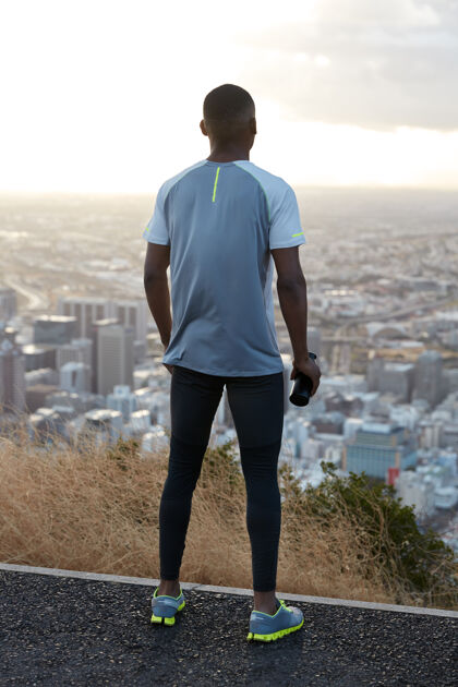 跑步者户外垂直拍摄的运动员穿着运动服 站在后面 从上面欣赏自然景观和城市景观 拿着运动水瓶 享受晨练健身理念风景天空裤子