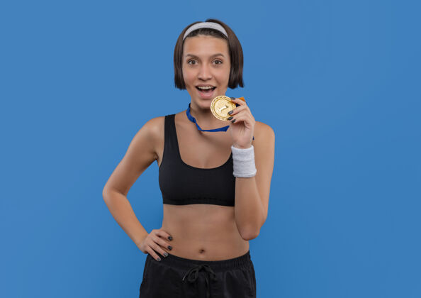 人物一位身穿运动服 脖子上挂着金牌的年轻健身女士高兴地站在蓝色的墙上走了出来运动脖子奖牌