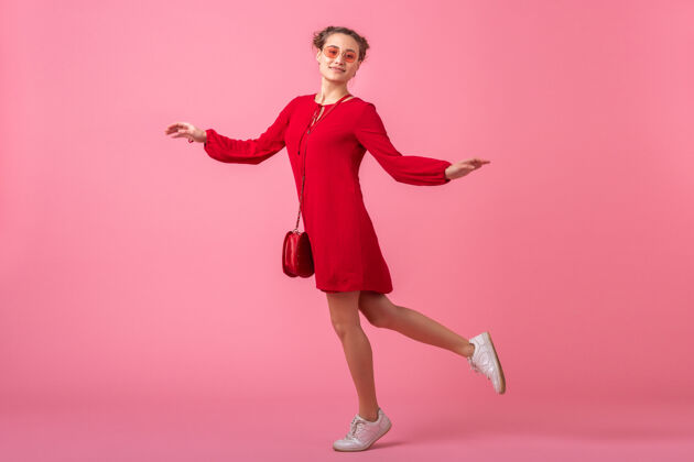 乐趣迷人的快乐微笑的时尚女人穿着红色的时髦连衣裙在粉色的墙上蹦蹦跳跳 春夏的时尚潮流 浪漫的情调撩人的女孩衣服颜色女孩