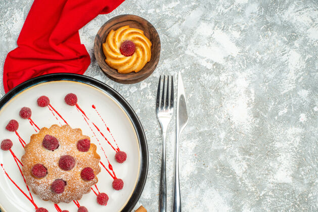 披肩俯瞰白色椭圆形盘子上的浆果蛋糕 红色披肩 灰色表面上的饼干叉和餐刀 复制空间景观饼干顶部