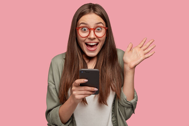 信息惊讶的高加索女孩手持现代手机 展示手掌眼镜设备手机