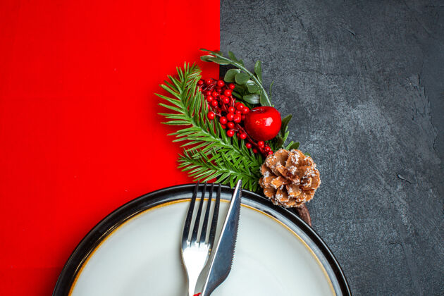 维管植物xsmas背景的半张照片 餐具套装 餐盘上有红丝带装饰配件 黑色桌子上红色餐巾上有杉木树枝灌木水果萝卜