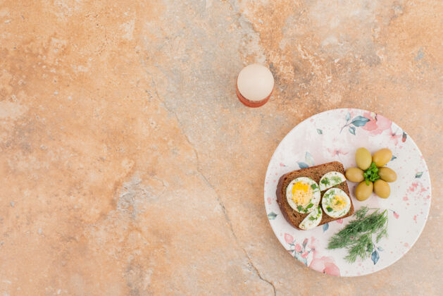 美味美味的吐司与煮熟的鸡蛋和橄榄在盘子里盘子食物吐司