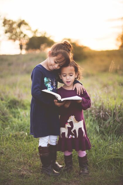 书两个可爱的小姐妹在公园里读圣经的垂直镜头可爱可爱童年