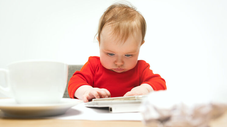 欢呼小女婴坐在白色工作室里 用现代电脑或笔记本电脑的键盘科技惊喜年轻
