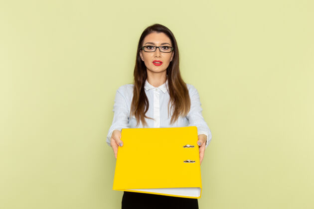 业务身穿白衬衫和黑裙子的女上班族手持黄色文件站在绿色墙上的正视图前面文件工作