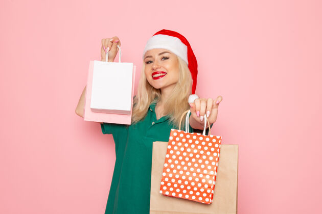 美丽正面图：年轻女性手持圣诞礼物包装在粉红色的墙上圣诞照片模型新年假期年轻女性购物者风景