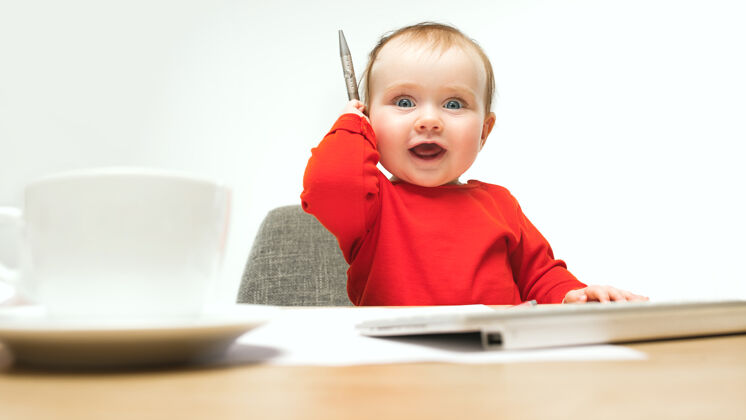 科技快乐的小女婴坐在一个白色的工作室里 用现代电脑或笔记本电脑的笔和键盘幼儿教育孩子