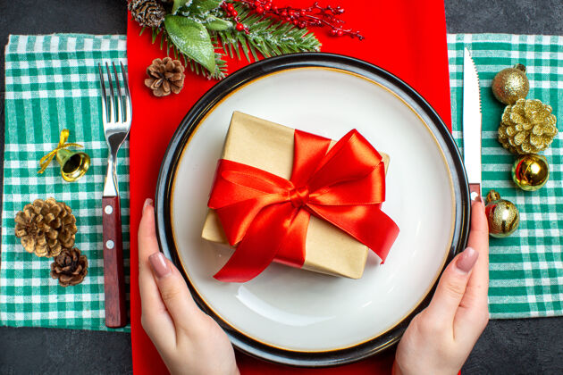 碗顶视图手拿着一个漂亮的礼品盒与蝴蝶结形状的红丝带在一个盘子和餐具集装饰配件绿色剥离毛巾圣诞节杯子视图
