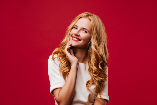 金发可爱的长发女孩在拍照时微笑快乐的笑妇站在红墙上情感迷人发型