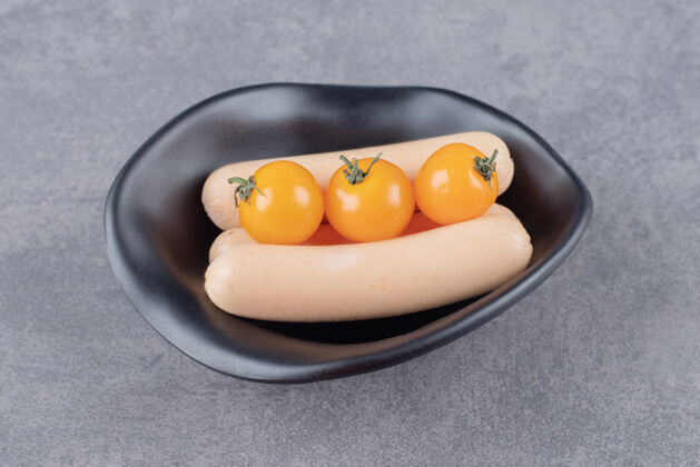 膳食一个黑色的盘子 里面有煮香肠和黄色的西红柿营养蛋白质蔬菜