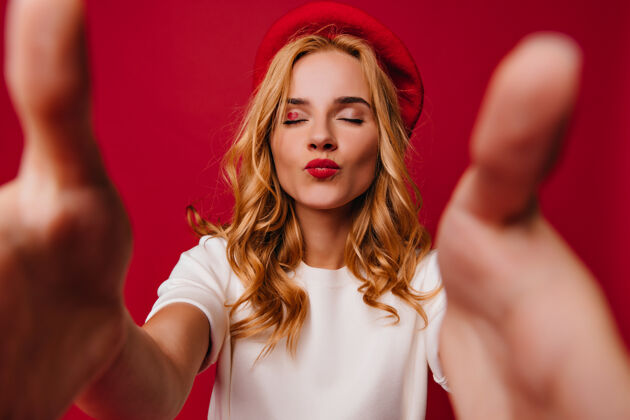 女人一个戴贝雷帽的漂亮女孩摆出亲吻的表情室内拍摄的穿着法国服装的可爱美女站在红墙上配饰微笑金发
