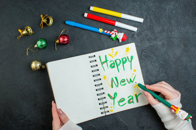 钢笔手持钢笔的螺旋笔记本俯视图 黑色背景上有新年快乐书写装饰配件书写圣诞节铅笔