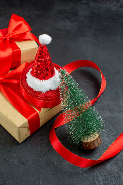 季节竖视美丽的礼物与红丝带和圣诞老人帽圣诞树在黑暗的桌子上节日帽子圣诞节