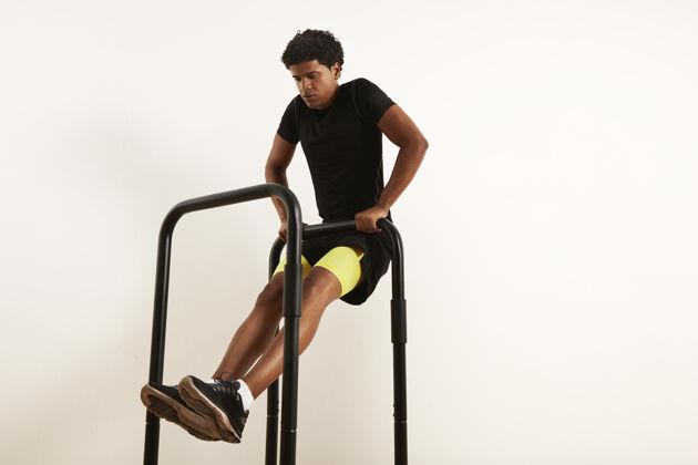交叉身穿黑色运动服的年轻非裔美国运动员 在白色隔离带上的移动吧台上表演体重排运动肌肉锻炼