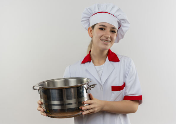 牙套面带微笑的年轻漂亮厨师穿着厨师制服 戴着牙套 拿着一个看起来孤立的罐子站在白色的空间里持有年轻