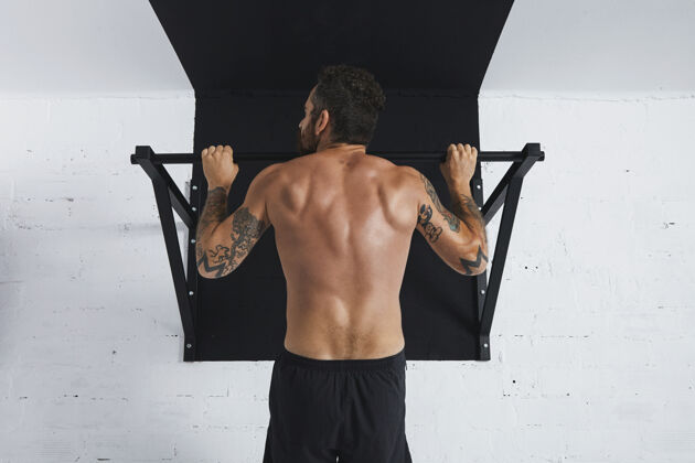 手肌肉发达的赤裸上身男运动员展示健美操动作的后视图在撑杆上向上拉 头部朝左侧方向看体格男性运动员