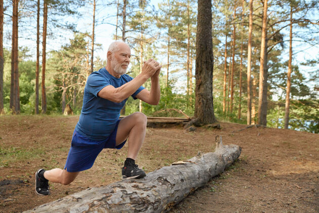 运动帅气精力充沛的老人 留着胡子 穿着运动服 在野外做有氧运动老人有着快乐自信的神情 脚踩木头 跑步前锻炼腿部肌肉活动森林原木