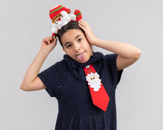 贴快乐的小女孩穿着针织连衣裙 头上系着一条红色领带 戴着一个有趣的圣诞戒指 露出舌头玩得很开心有圣诞快乐女孩