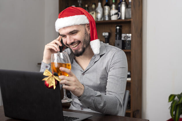 专业特写镜头一个西班牙裔男子戴着圣诞老人的帽子 享受他的酒和电话交谈电话玻璃聚会