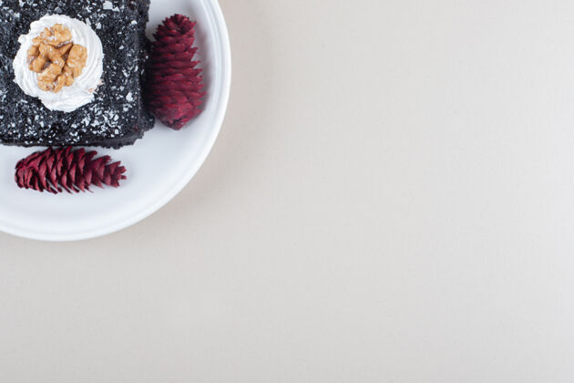 奶油巧克力蛋糕和红色松果放在大理石背景的盘子里配料糕点烘焙