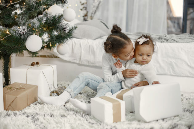 儿童穿着白色毛衣的孩子女儿们在圣诞树旁缝线两个姐妹在家灯童年女儿