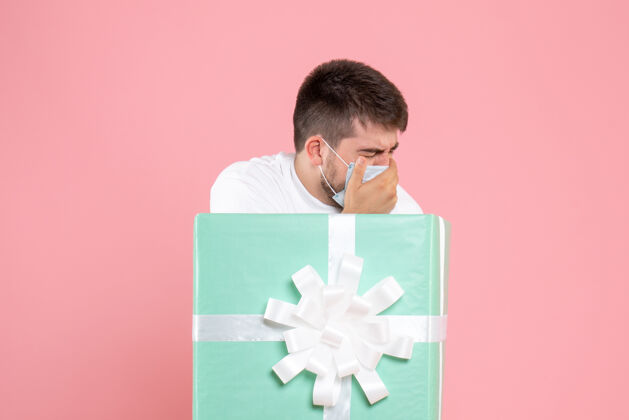 圣诞节粉红色墙上戴着病假面具的盒子里的年轻人的正视图感觉里面礼物