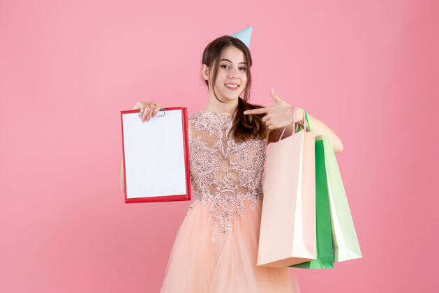 派对戴着派对帽的快乐女孩 手里拿着文件和粉红色的购物袋快乐粉色模特