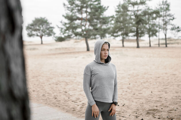 运动户外图片：身材苗条的年轻女子穿着时尚的运动服 在沙滩和松树的背景下 在户外摆姿势 锻炼身体 做晨练选择重点运动健身健康