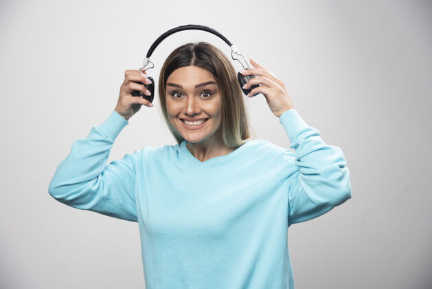 年轻穿着蓝色运动衫的金发女孩拿着耳机 准备戴上耳机听音乐音乐积极娱乐