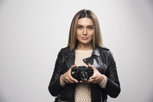 数码穿着黑色皮夹克的年轻女士严肃而专业地用相机拍照创意设备摄影