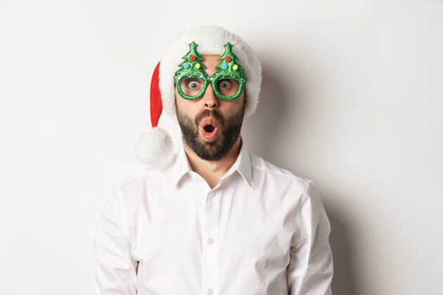 欢快庆祝寒假的成年男子 戴着圣诞派对眼镜和圣诞帽 惊讶地看着镜头 站着商人快乐男人