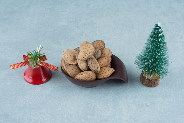 节日一碗去壳的杏仁和大理石上的圣诞装饰品小雕像铃铛天然