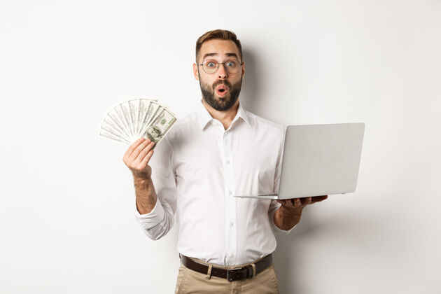 印象深刻商业和电子商务男人看着惊奇的金钱收入 在线工作 使用笔记本电脑 站着富人办公室惊讶