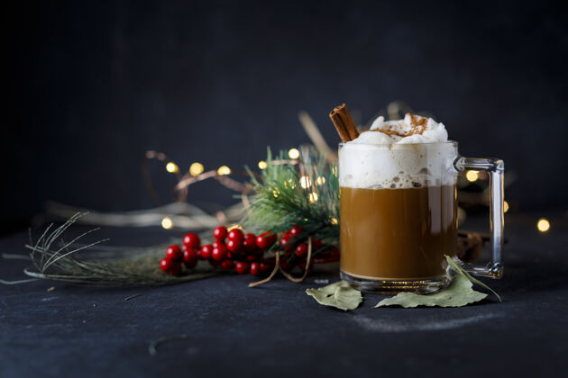 令人愉快美味的圣诞咖啡 肉桂和泡沫 旁边的冬青在黑暗的表面杯子植物卡布奇诺