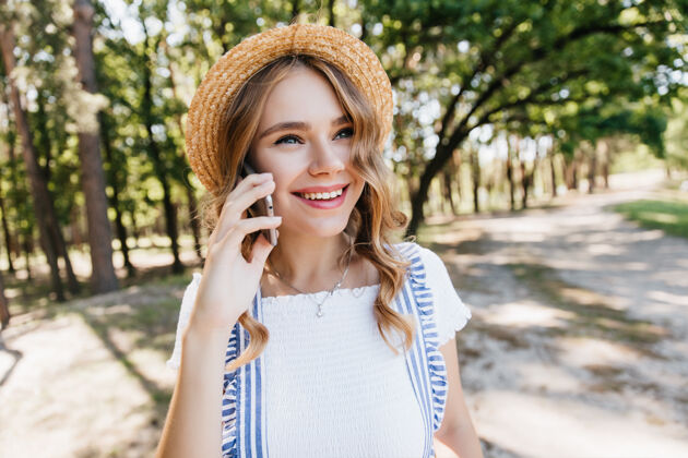 户外幸福的年轻女士戴着时髦的草帽 在电话交谈中微笑着神奇的白人女孩打电话给朋友的户外照片年轻休闲户外