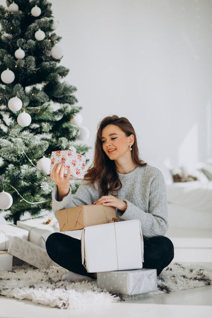 欢笑在圣诞树旁拿着圣诞礼物的年轻女子装饰圣诞盒子圣诞