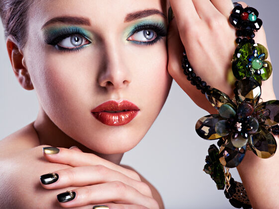 化妆漂亮的女人脸 手上有时尚的绿色化妆品和珠宝手指眼睛华丽