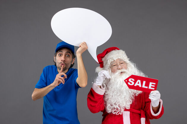 圣诞老人圣诞老人与男信使手持白色标志和灰色墙上的销售横幅的正面视图人圣诞快乐工作