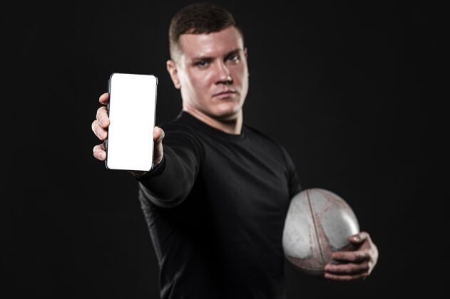 人男性橄榄球运动员手持球和智能手机的正面视图联系运动橄榄球
