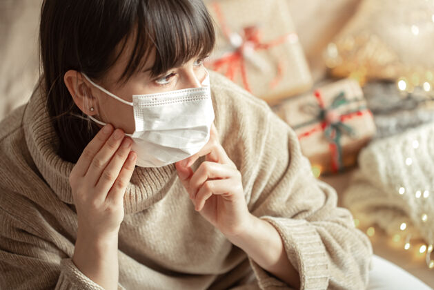 节日穿着舒适的米色毛衣 脸上戴着面具的年轻女子女人病毒感染